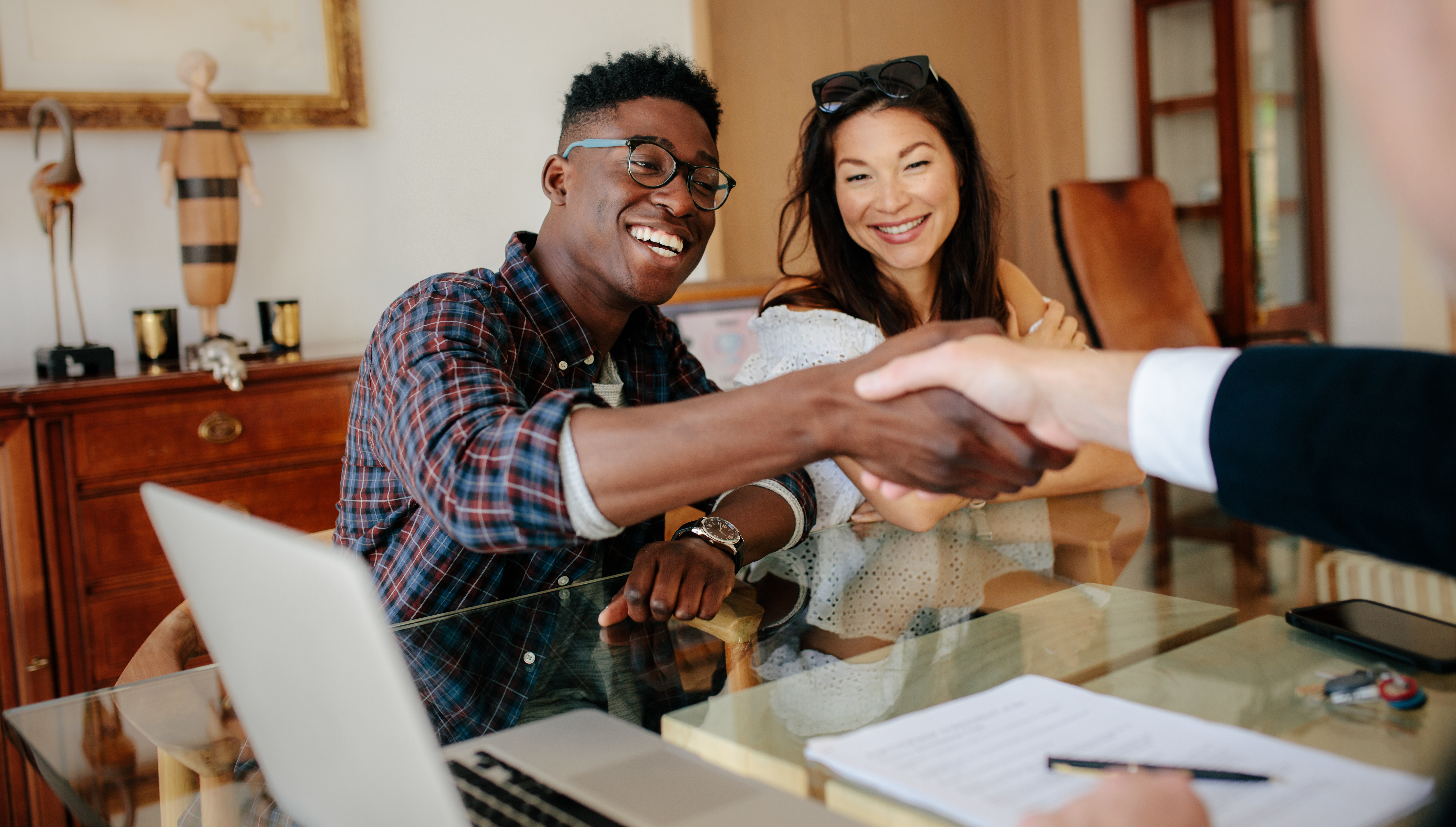 Couple shaking hands with another person at a desk. 